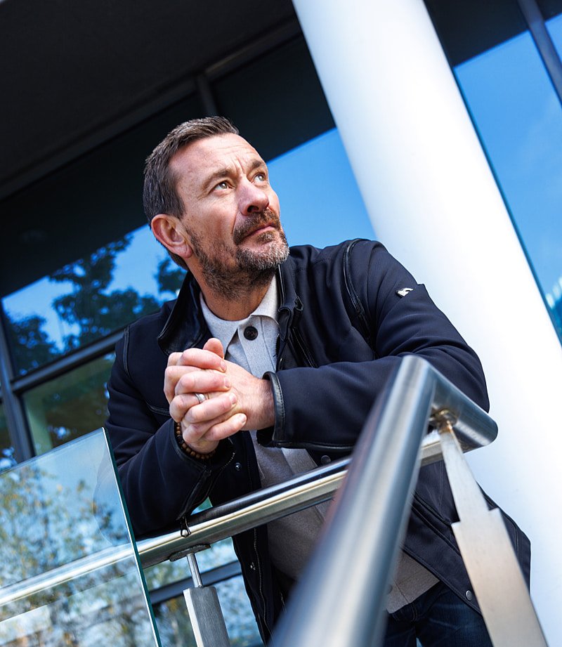 Ollie Ollerton, Founder of BreakPoint. Stood leaning against metal barrier and looking away from camera.